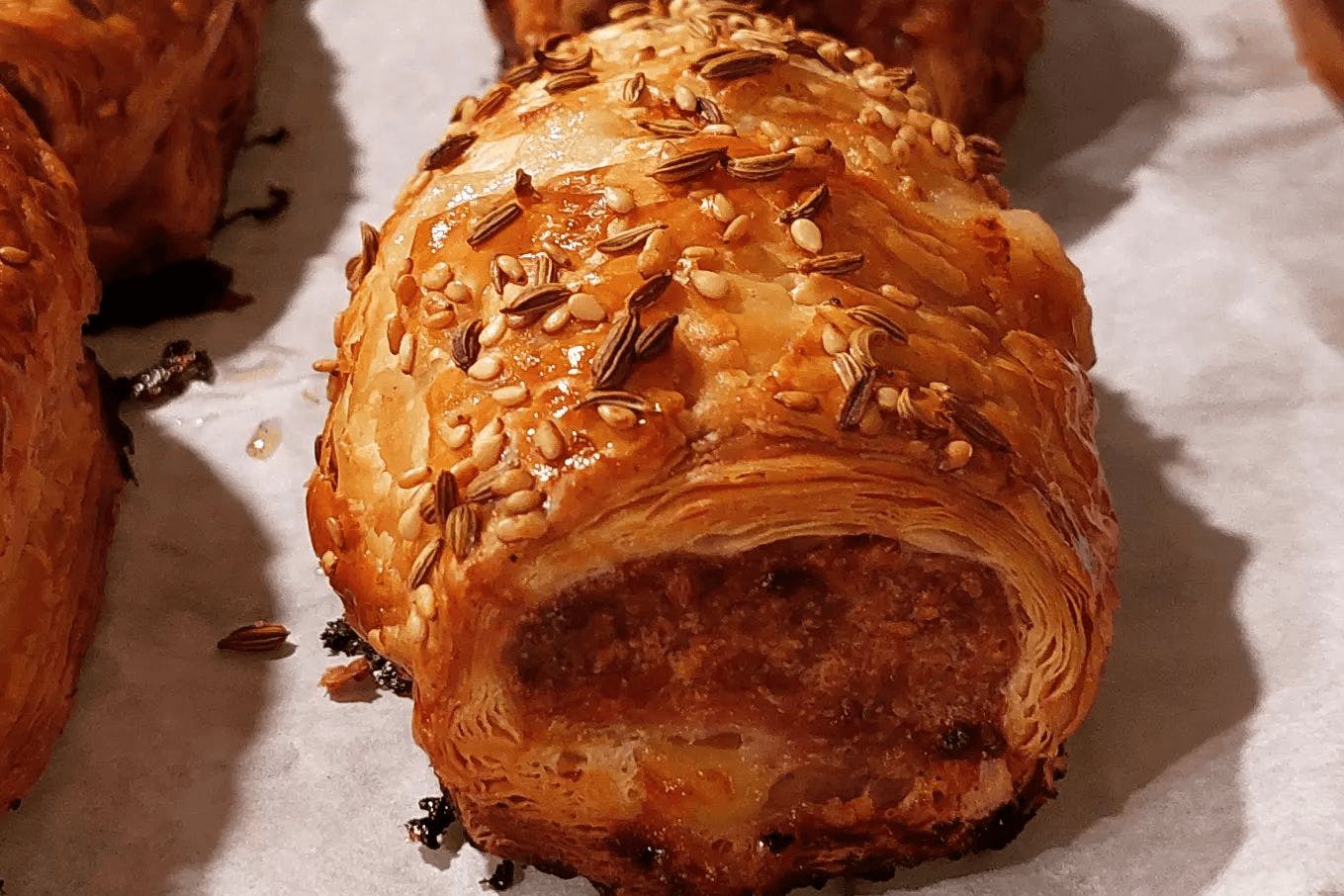 A thick sausage roll with sesame and fennel seeds on top.